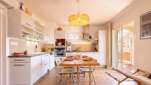 A modern kitchen with white cabinets, a wooden dining table, and a hanging light fixture.