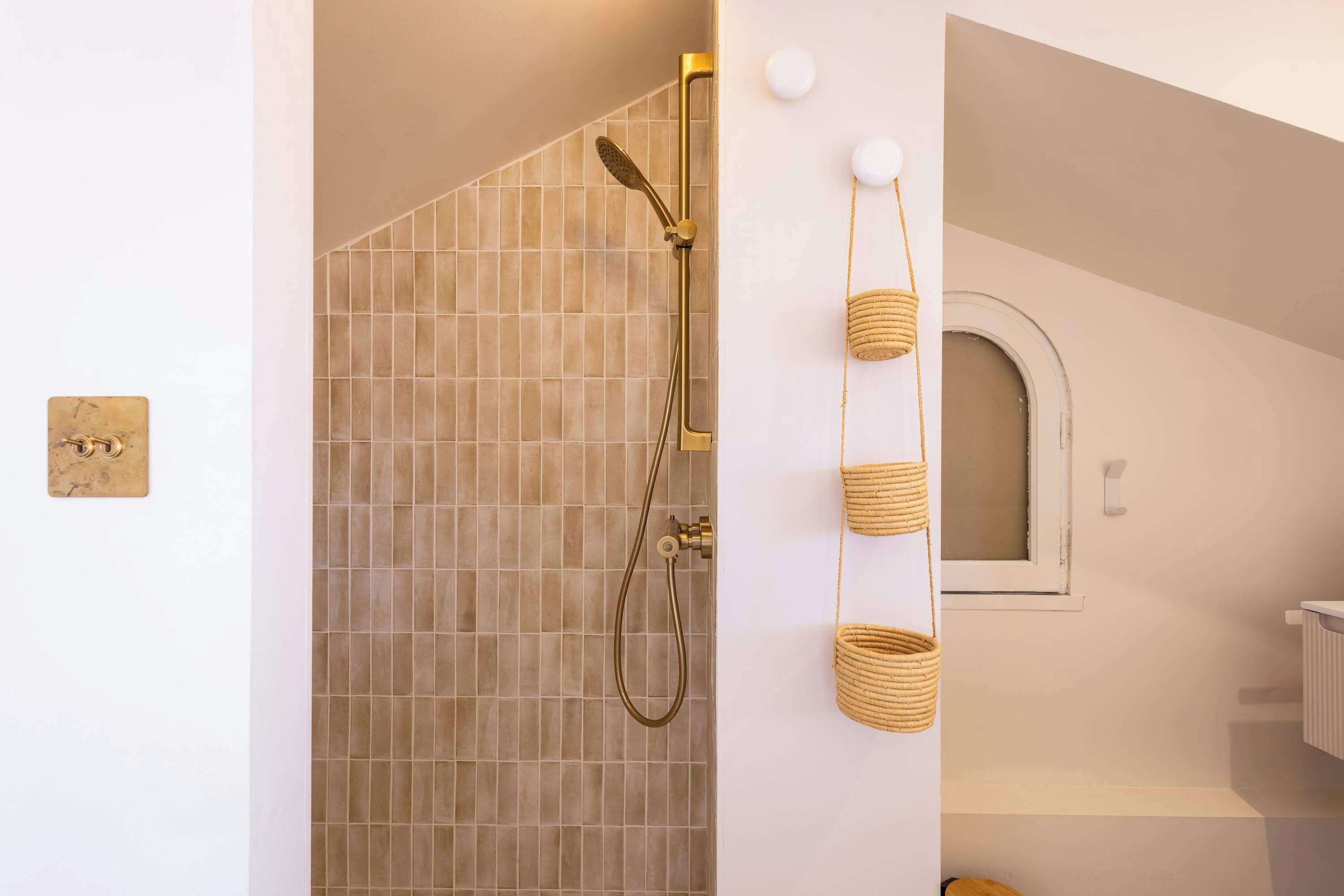 A bathroom with a shower, tiled walls, a small window, and a wall-mounted light fixture.