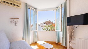 A room with a bed, a small table, a TV, and a window with curtains. - Comfort & Charm – 1-Min Walk to the Sea (Valras-Plage)