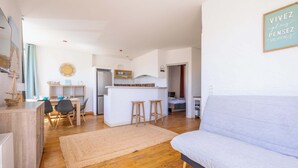 A modern living room with a sofa, a dining area with chairs and a table, a kitchen area with a fridge and a counter, and a wall with a motivational quote. - Comfort & Charm – 1-Min Walk to the Sea (Valras-Plage)