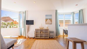A living room with a sofa, a TV, a wooden cabinet, a dining table, and a view of the outside. - Comfort & Charm – 1-Min Walk to the Sea (Valras-Plage)