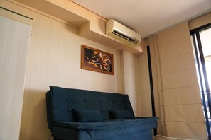 Ένα δωμάτιο με έναν μπλε καναπέ, μια μονάδα κλιματισμού στον τοίχο και έναν πίνακα με κορνίζα τοποθετημένο πάνω από τον καναπέ.
