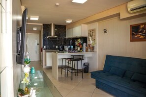 Un salon moderne avec un canapé bleu, un coin cuisine doté d’un pare-feu en marbre et un espace repas avec deux tabourets de bar.