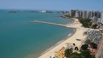 A coastal cityscape with a sandy beach, a long pier, and high-rise buildings.