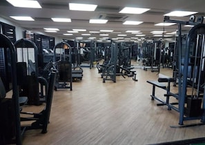 A gym with various exercise machines, wooden flooring, and overhead lighting. - Beira Mar Fortaleza Landscape Luxo (Fortaleza)