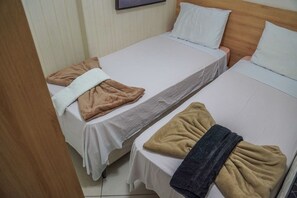 Deux lits simples avec du linge de lit blanc, chacun étant agrémenté d’une couverture marron et d’une serviette blanche.