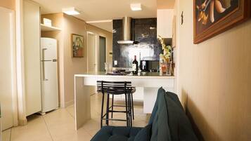A modern kitchen with a white countertop, a stainless steel range hood, and a bar area with a wine bottle and glasses.