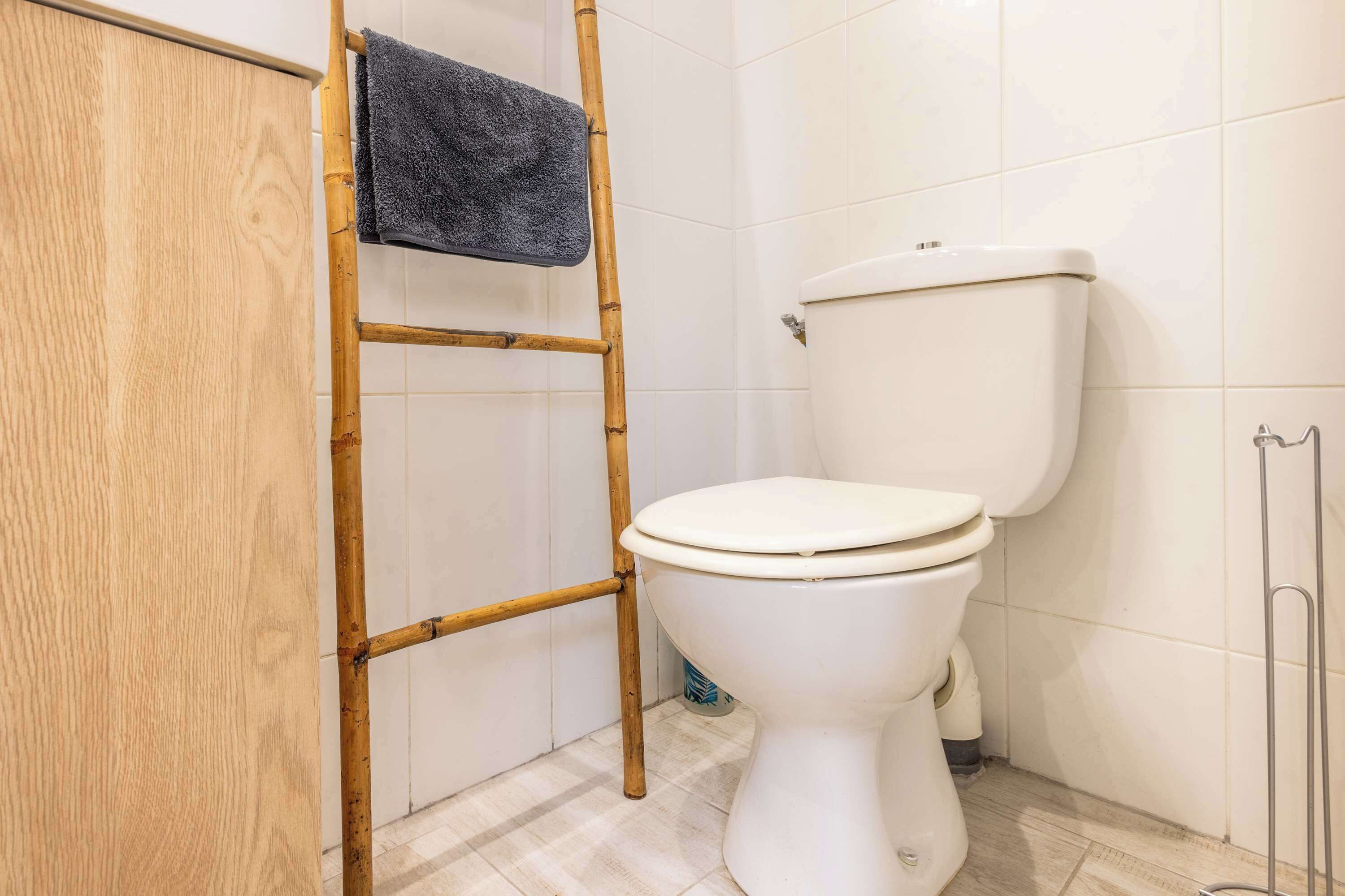 Ein Badezimmer mit Toilette, einem Holzkabinent, einer Bambusleiter und einem Handtuch, das am Kabinent hängt.