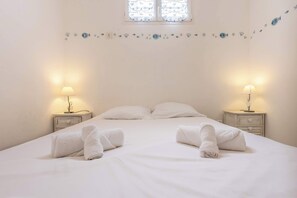 Un lit bien fait, avec deux oreillers, deux tables de chevet avec des lampes et un motif décoratif représentant des poissons sur le mur.