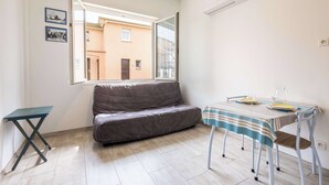 Et værelse med en sofa, et spisebord med stole, et lille bord, et vindue og en vægmonteret klimaanlæg.