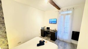 A hotel room with a bed, a desk with a laptop, a television, and a window with curtains. - Orb Room – 1st Floor (Béziers)