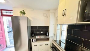 Eine kompakte Küche mit Kühlschrank, Herd, Mikrowelle und einer kleinen Arbeitsfläche mit einer Pflanze.