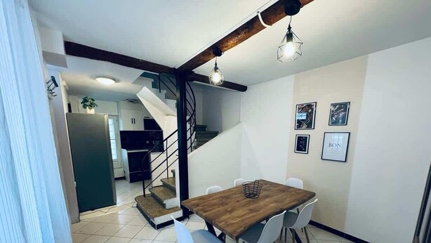 Ein Essbereich mit Holztisch und weißen Stühlen, eine Treppe und eine Küche im Hintergrund.