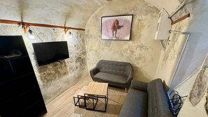 Una habitación rústica con piso de madera, un sofá gris, una pequeña mesa de madera, un mueble negro y un televisor montado en la pared.