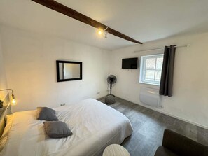 A bedroom with a bed, bedside lamp, wall-mounted TV, and a window with curtains.