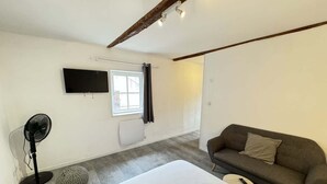 Un dormitorio con cama, sofá, ventilador, televisor y ventana.