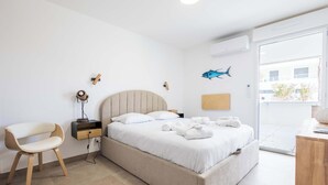 A modern hotel room with a large bed, a bedside table, a chair, and a view of the outside. - Beachfront Apartment w/ Terrace, Hot Tub & Parking (Valras-Plage)
