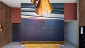 A modern interior with a wooden bench, a wall-mounted sign reading "ARCHIPEL", and a ceiling light fixture. - Beachfront Apartment w/ Terrace, Hot Tub & Parking (Valras-Plage)