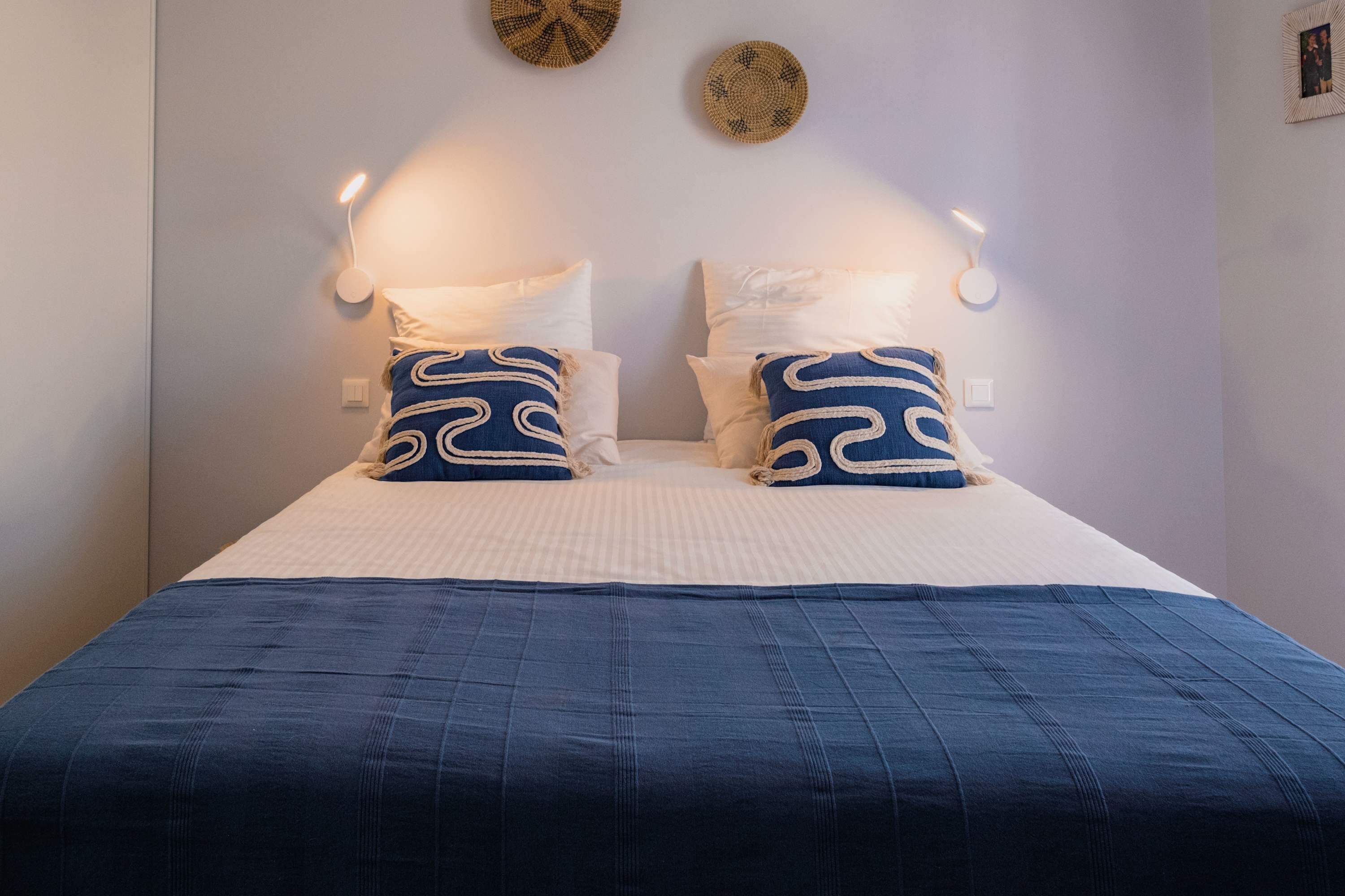 Een net opgemaakt bed met een blauwe sprei en twee kussens met een wit en blauw dessin.