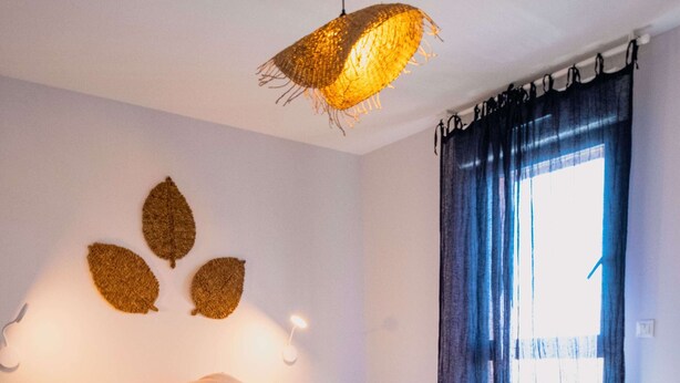 Une chambre à coucher avec un lit, des lampes de chevet, un luminaire suspendu et une fenêtre avec des rideaux.