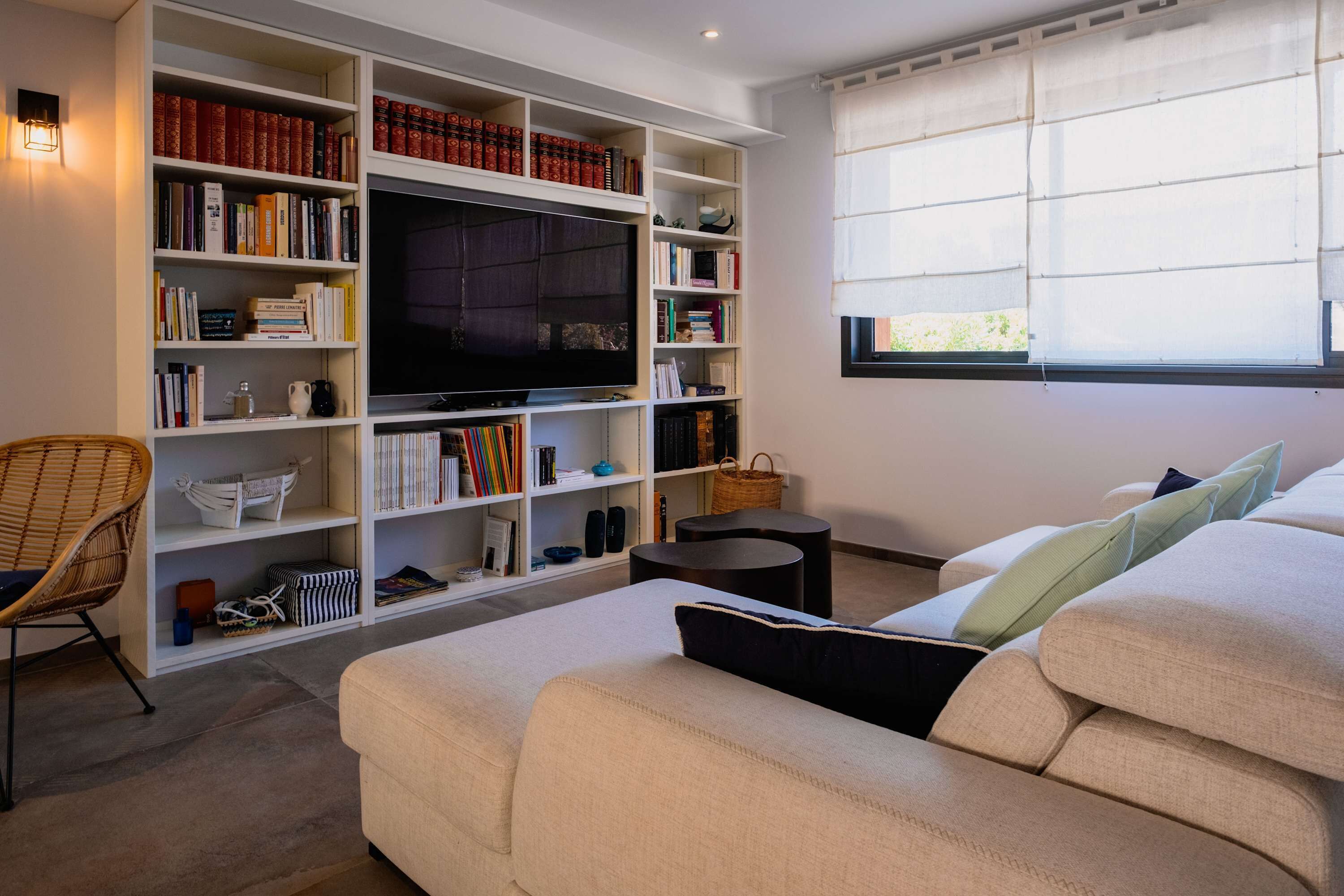 Un salon doté d’un grand téléviseur à écran plat, d’une bibliothèque remplie de livres, d’un fauteuil en osier et d’un canapé agrémenté de coussins.