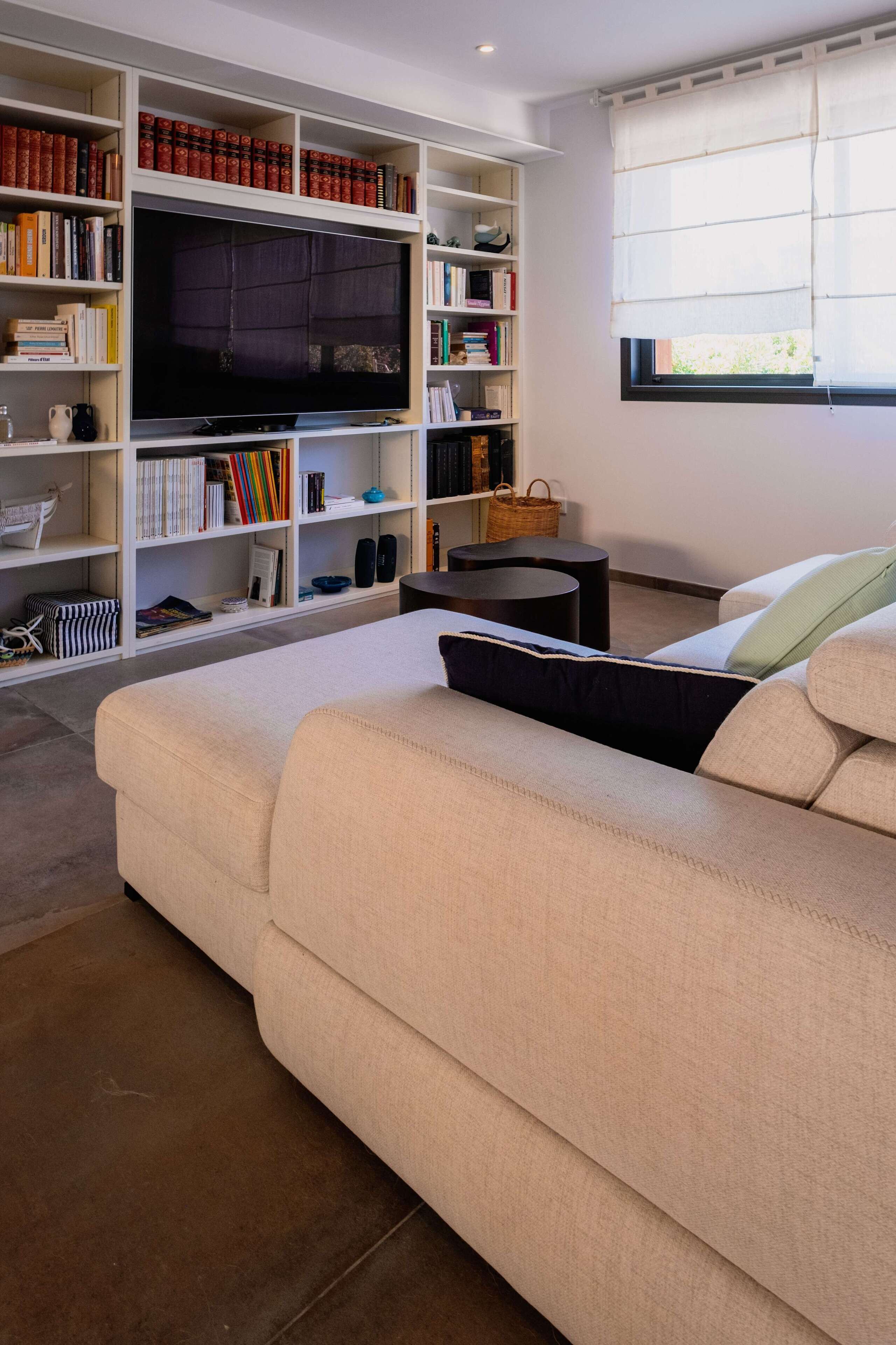 A living room with a beige sofa, a flat-screen TV, and a bookshelf filled with books and decorative items.