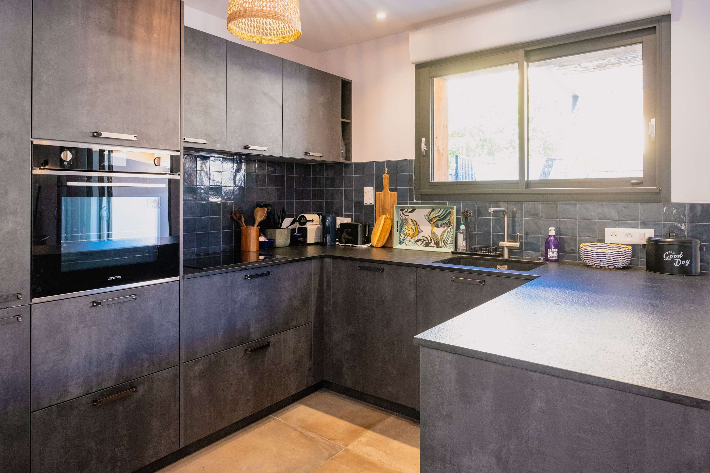 A modern kitchen with dark cabinetry, a built-in oven, and a large window.