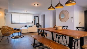 Un salon moderne avec une table à manger en bois, des bancs, des chaises en osier et un canapé.