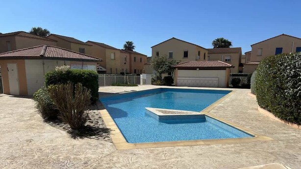 A swimming pool with a tiled deck, surrounded by residential buildings and greenery.