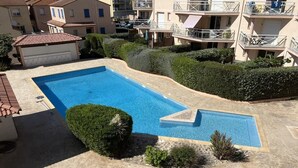 A rectangular swimming pool with a small adjacent section, surrounded by a landscaped area with bushes and a tiled deck.