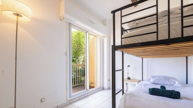Una stanza con un letto a castello, un comodino, una lampada, una finestra vista sul verde e una porta scorrevole.