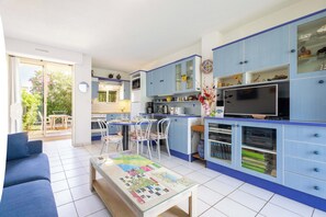 A modern kitchen with blue cabinets, a dining area with chairs, and a sofa in a living room.