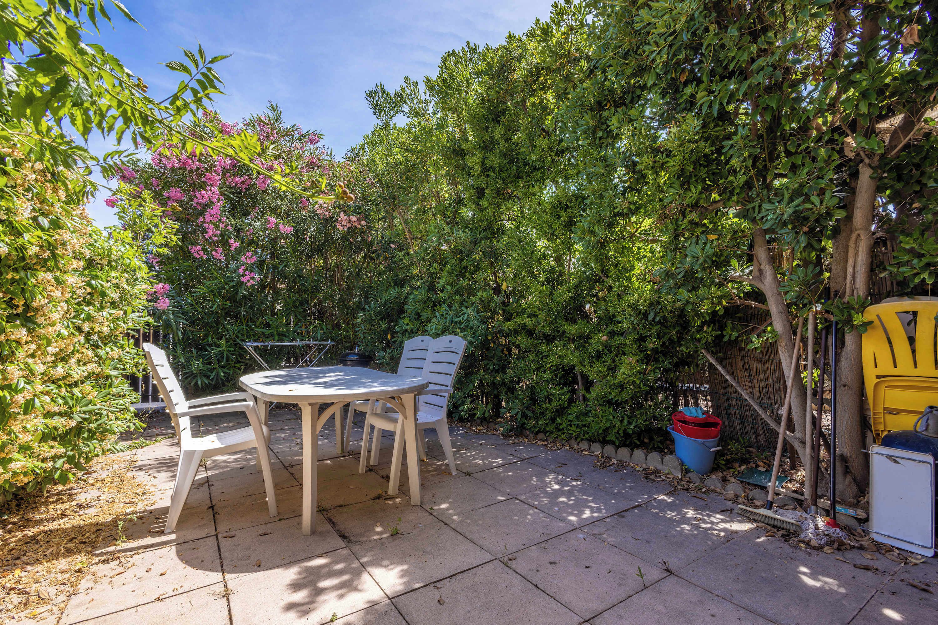 Een terras met een tafel en stoelen, omringd door weelderige beplanting en een kleine boom.
