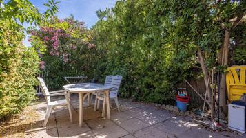 Een terras met een tafel en stoelen, omringd door weelderige beplanting en een kleine boom.