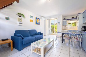 A living room with a blue sofa, a glass coffee table, and a dining area with chairs.