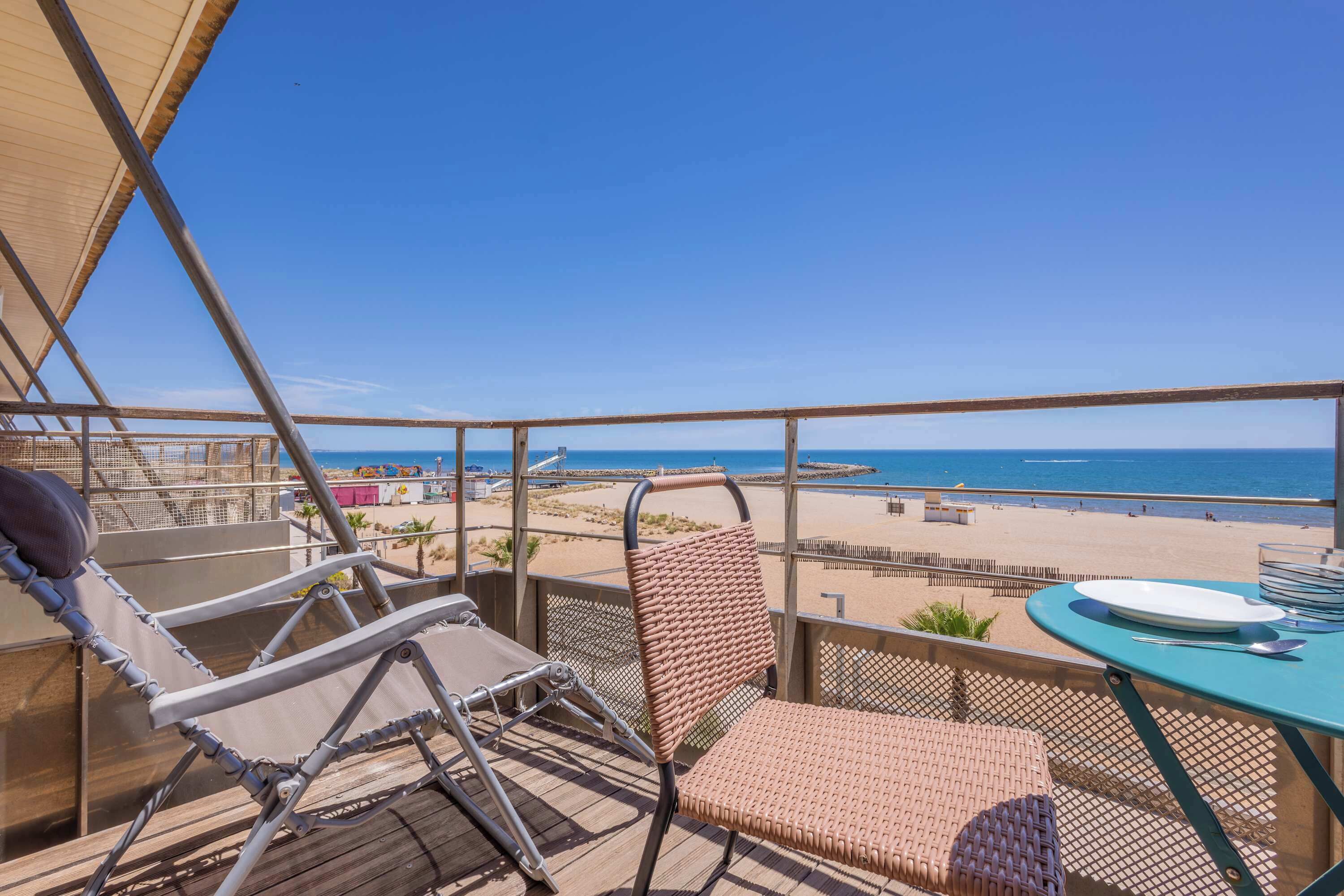 Un balcon donnant sur la plage, une table avec une assiette et deux chaises.