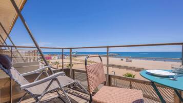 Un balcon donnant sur la plage, une table avec une assiette et deux chaises.
