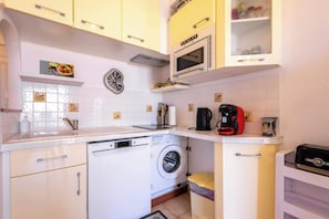 A compact kitchen with a washing machine, microwave, and coffee maker. - Valras’Loc Seafront with Stunning Sea View (Valras-Plage)