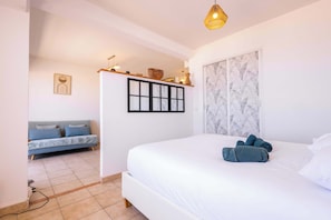 A bedroom with a bed, a sofa, a wall-mounted shelf with decorative items, and a framed picture. - Valras’Loc Seafront with Stunning Sea View (Valras-Plage)