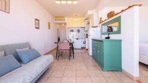 Un espace de vie compact comprenant un canapé, une table à manger, un coin cuisine et un meuble vert.