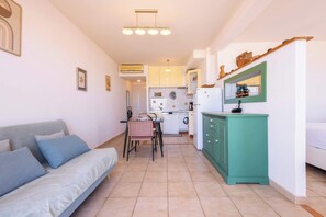 Un espace de vie compact comprenant un canapé, une table à manger, un coin cuisine et un meuble vert.