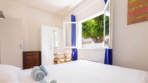 A hotel room with a bed, a wooden nightstand, a desk with chairs, a window with blue curtains, and a wall with motivational text.