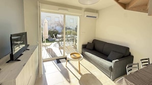 Ein modernes Wohnzimmer mit einer Couch, einem Fernseher, einem kleinen Tisch und einer Glastür, die auf eine Terrasse im Freien führt.