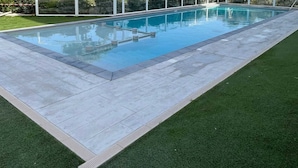 Ein rechteckiger Schwimmteich mit einer gefliesten Liegefläche und einer umlaufenden Rasenfläche.