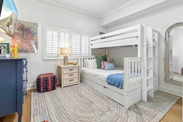 Habitación infantil con literas, un escritorio, una silla, una lámpara y una ventana con persianas.