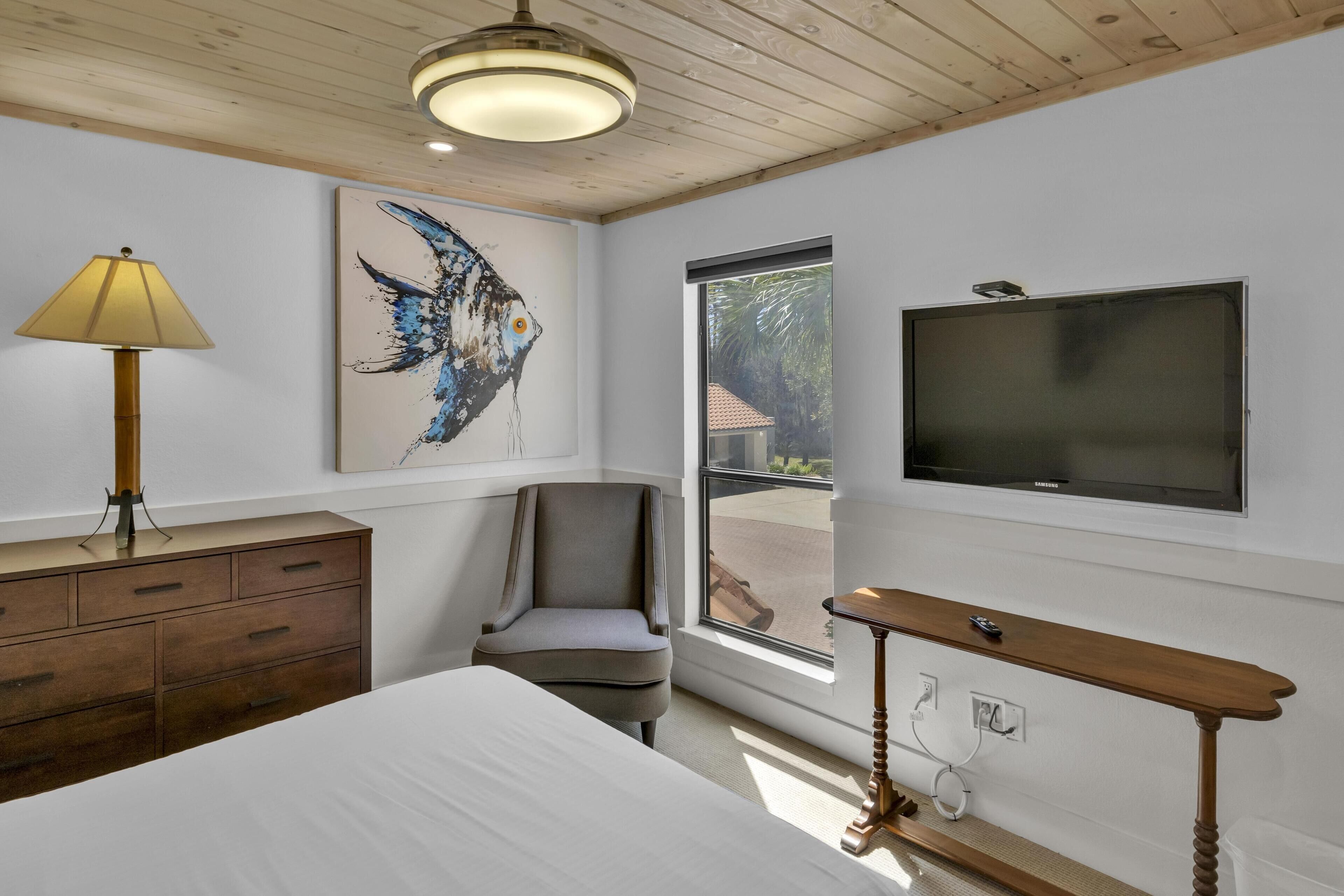 A bedroom with a bed, a desk, a chair, a lamp, a TV, and a window with a view.