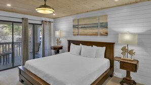 Un dormitorio con una cama grande, cabecera de madera, dos mesitas de noche con lámparas, un ventilador de techo y vistas al exterior a través de una puerta corrediza de vidrio.