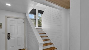 Un interior en tonos blancos con una escalera de madera y una puerta con cerradura electrónica.