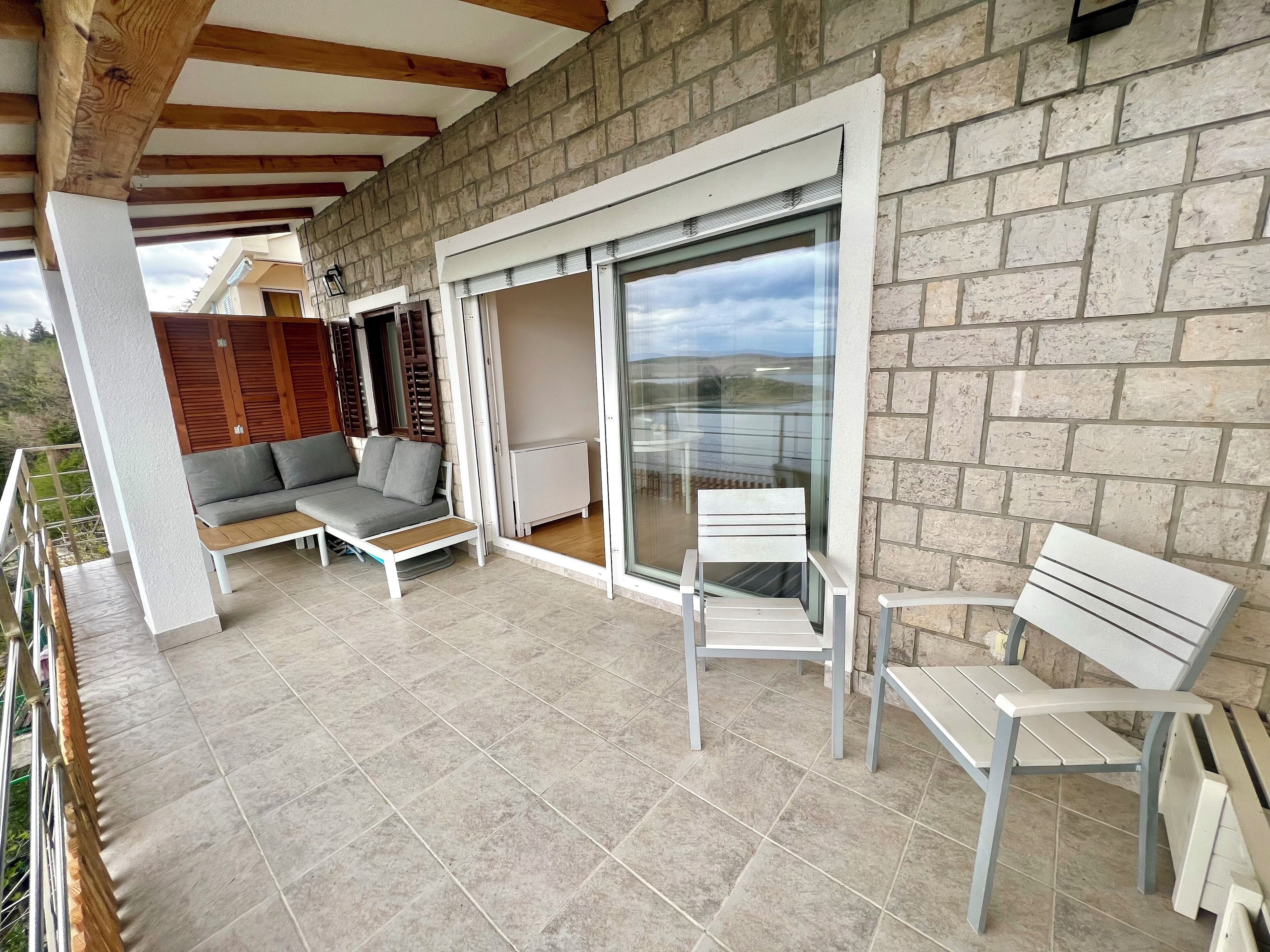 A balcony with a stone wall, a grey sofa, and two white chairs.