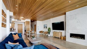 Een moderne woonkamer met een houten plafond, een grote televisie en een open haard.